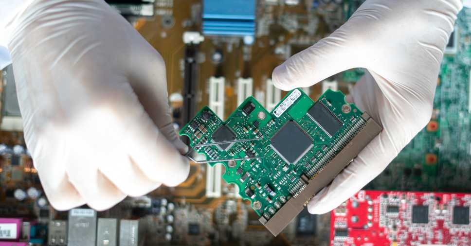 Mãos de luva seguram placa eletrônica limpa com a pureza do álcool isopropílico.